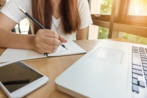 woman with long hair writing notes next to a computer