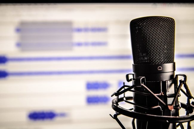 Image shows a studio microphone in front of a computer screen displaying audio waves