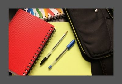 Images shows red, yellow and multi-coloured striped notebooks beside a laptop case with blue and black pens on top