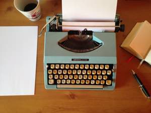 Image shows an old typewriter and pages on desk