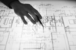 Image shows a silhouetted hand using a pen to point at construction blueprints