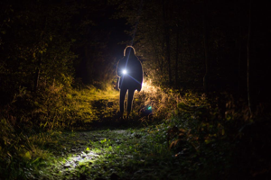 Image shows a figure at night holding a torch walking over grass towards the camera