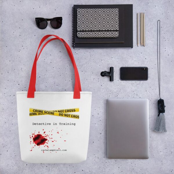 Image shows tote bag with red strap and yellow crime scene tape with the words Detective in Training underneath and blood spatter