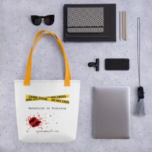 Image shows tote bag with yellow strap and yellow crime scene tape with the words Detective in Training underneath and blood spatter