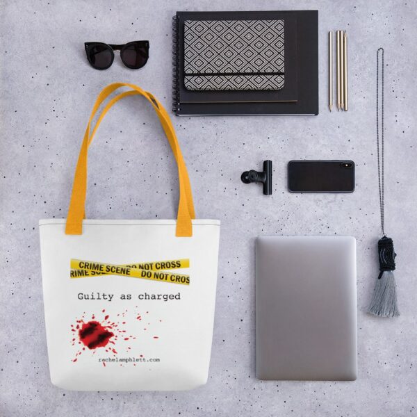 Image shows tote bag with yellow strap and yellow crime scene tape with the words Guilty as Charged underneath and blood spatter
