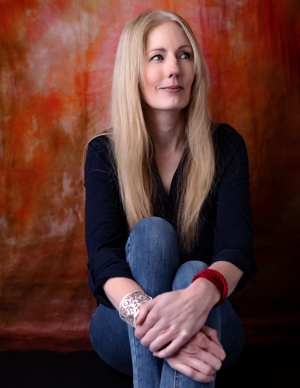 Rachel Amphlett 300×388 Author photo of Rachel Amphlett wearing a blue shirt against an orange background while she looks to the left of the image